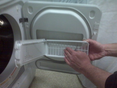 The lint trap is shown freed from the door and open, with hands removing the lint from it.