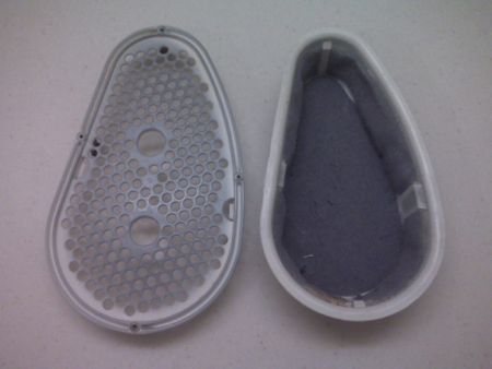 A Whirlpool dryer lint trap sits on a table, opened into two pieces. The cover is on the left side with the catcher, full of lint, on the right.