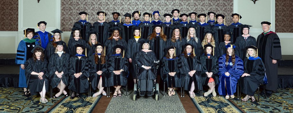 A large group of people in graduation gowns are seen in a conference center lobby. They are graduate students at Penn State College of Medicine, in May 2018.