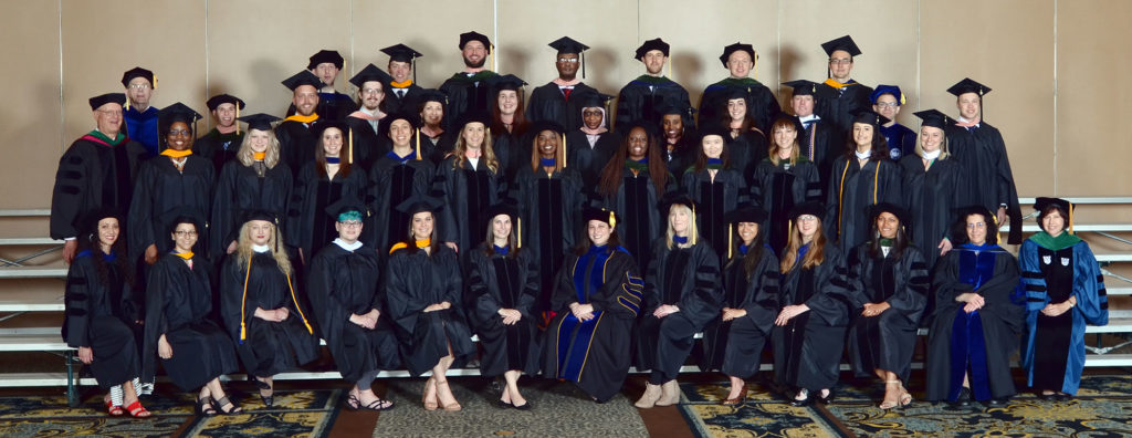 A large group of people in graduation gowns are seen in a conference center lobby. They are graduate students at Penn State College of Medicine, in May 2019.