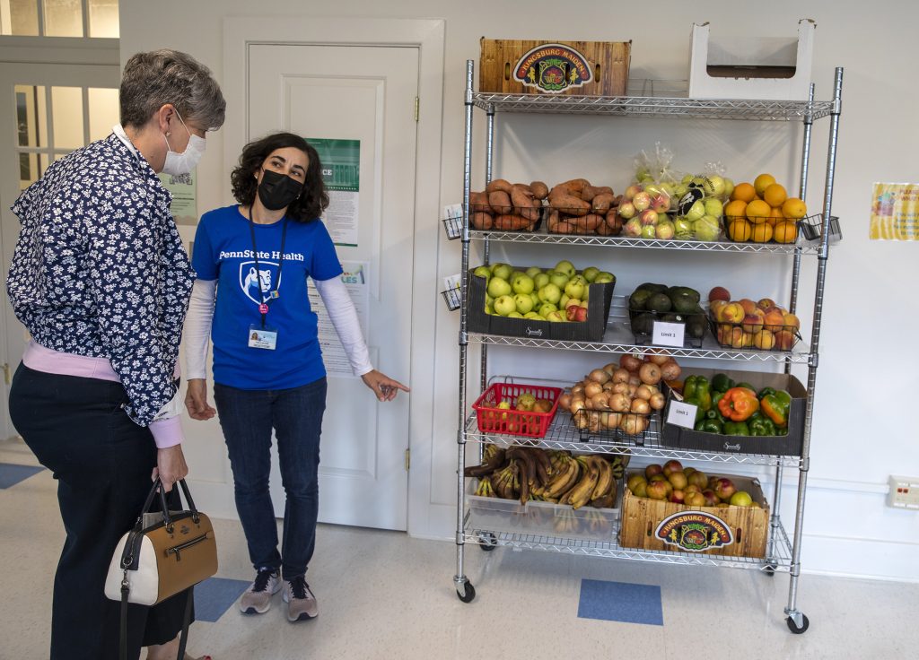 Paula Moodie, research project manager at Penn State College of Medicine, points to a shelving unit full of fruit and vegetables at the Student and Employee Food Pantry as Sheilah Borne, associate Vice president for Governmental Health Relations for Penn State Health, looks on.