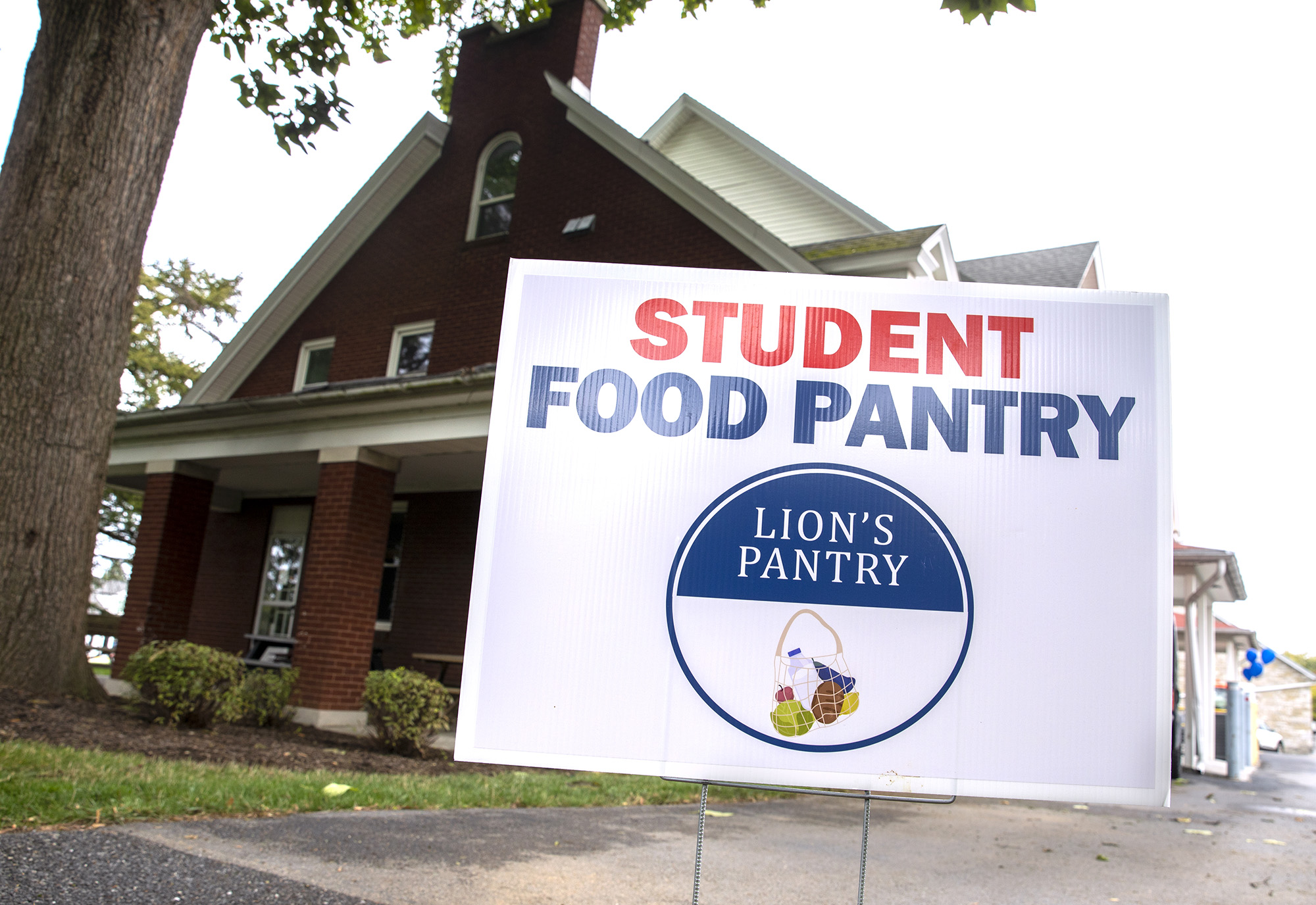 A sign that says "Student Food Pantry" and "Lion's Pantry" in a circle logo stands in front of the Student and Employee Food Pantry at 922 West Governor Road.